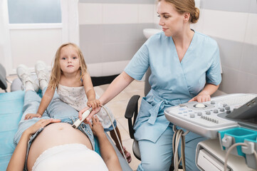 Happy doctor pregnant mother's ultrasound visit, sharing excitement with daughter who eagerly...