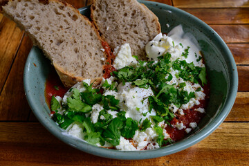 Shakshouka Poached Eggs in a Spicy Tomato Sauce with Feta Cheese, Cilantro and Fresh Bread, an Maghrebi Brakfast Dish