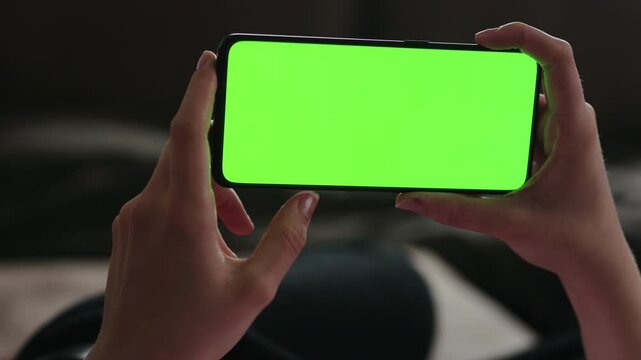 Young woman lying on a couch and using smartphone with horizontal green screen