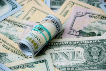 Hundred dollar bills roll lies on big amount of US dollars in different nominations under natural light