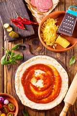 Raw pizza dough with tomato sauce and basil leaves.