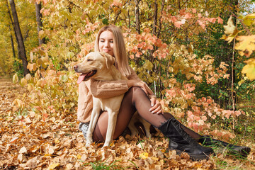 A young woman walking with her beloved labrador dog in autumn park.