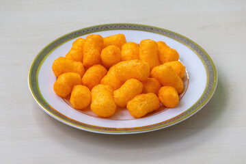 Tasty cheese flavored snacks crackers chips on a white plate on light a wooden surface.