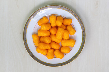 Crispy cheese flavored snacks crackers chips on a white plate on light a wooden surface. Top view.