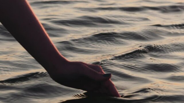 Slow motion closeup young female hand draws water at sunset