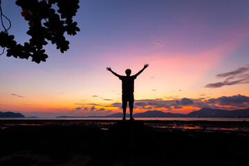 Silhouette of man raised his hands with tree frame at sunset or sunrise sky