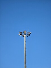 A tall metal streetlight with multiple lamps set against a clear blue sky. The minimalist composition highlights the modern urban infrastructure and clean background.