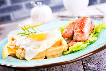 Delicious breakfast. Served on a wooden table with toast, eggs, sausage, wafers, juice.