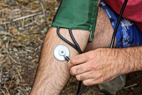 green medical rubber cuff with black hoses and iron round phonendoscope placed on patient's arm to measure blood pressure during daytime outdoors - Powered by Adobe