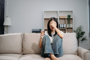 Asian woman sit Depression Dark haired  pensive glance Standing by window and anxiety Copy space with a blanket on a sofa.