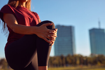 Young woman stretching after exercise and jogging in urban park during sunny summertime day.