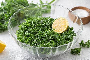 Chopped kale cabbage leaves with lemon in a transparent bowl on a light gray background