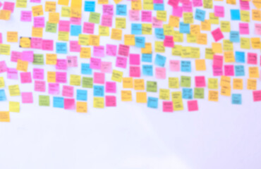 Blurred background of many colorful sticky notes with lots of text on white wall for backdrop design