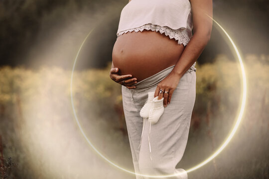 Pregnant woman's belly holding baby shoes