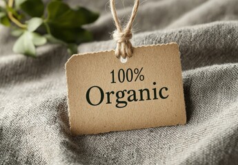 A tag stating 100% organic rests on textured fabric with leaves nearby, highlighting sustainability