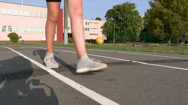 A girl in a sports uniform and shoes stretches her legs before jogging, close-up