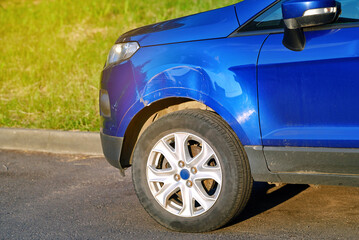 Car with front end damage in parking lot, front fender with large dent and visible scratches on...