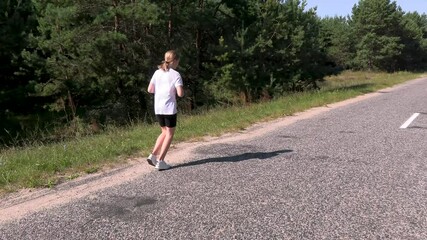 A young girl in a sports uniform runs a marathon near the forest on the road