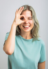 Fototapeta premium Happy young student shows ok sign with hand on eye looking through fingers