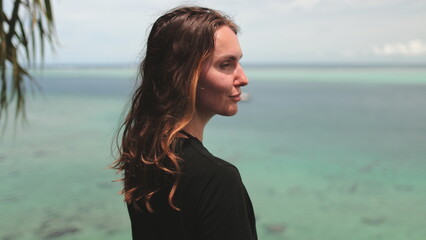 A woman stands in front of a body of water, appearing contemplative and connected to the natural...