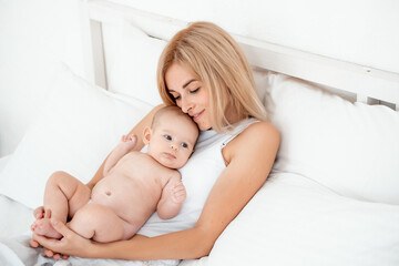 mom and baby hug and kiss, a young mother gently hugs a newborn baby girl holding her in her arms on the bed, maternal love and care, mother and daughter, a place for text.