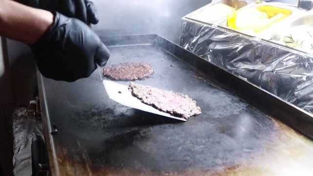 Video of a unrecognizable person flipping a smash burger on a griddle in a restaurant kitchen during food preparation