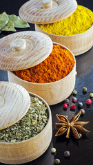 fragrant seasonings, multi-colored spices, in a wooden dish on a black table. cooking. black red and allspice, Illicium verum, ginger, basil and other spices in the kitchen. natural ingredients