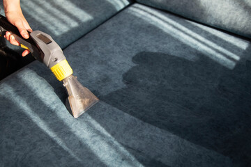 Cleaning the sofa from dirt with a washing vacuum cleaner. Cleaning company services, business. Copy space for text