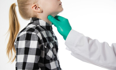 The hand of a pediatrician doctor probes the sore throat of a seven-year-old girl who has a sore throat. Inflammation of the lymph nodes, bacterial and viral infection. Copy space for text