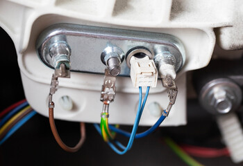 An electric heating element with a thermostat is connected with electrical chips. Repair and replacement of temperature sensor and heating element, hard water, close-up