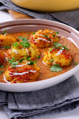 Malai Kofta served with yogurt and fresh herbs. Hot meal with potato and paneer cheese balls in tomato sauce. Indian cuisine