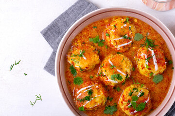 Malai Kofta served with yogurt and fresh herbs. Hot meal with potato and paneer cheese balls in tomato sauce. Indian cuisine. Top view