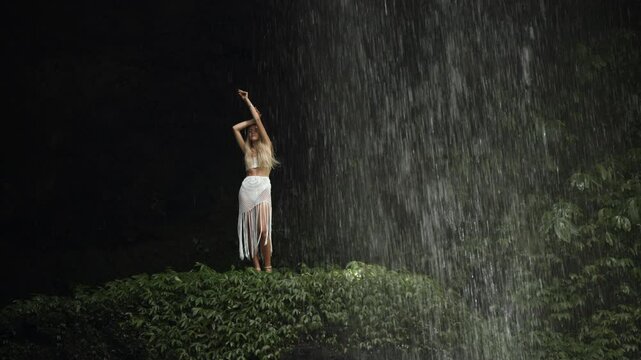 Beautiful woman in a white dress posing underneath a waterfall