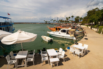 A charming cafe with white umbrellas and tables overlooking a bustling harbor in Side, Turkey.