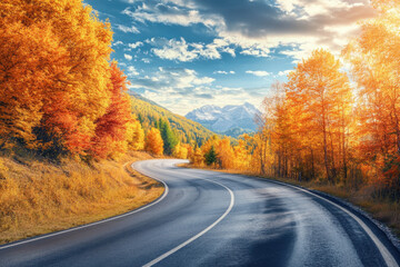 Naklejka premium Asphalt road is winding through a forest with colorful autumn foliage and mountains in the background