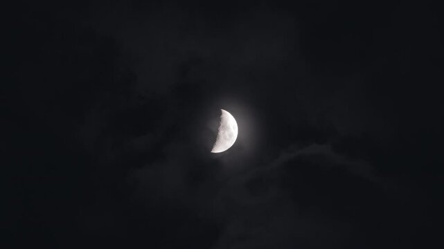 Moon in first quarter phase surrounded by misty dark clouds