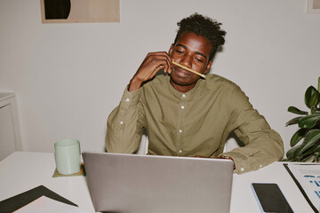 Tired male office worker sitting at table and looking at laptop screen