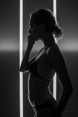 A woman in a black bikini is standing in front of a wall with a light shining on her