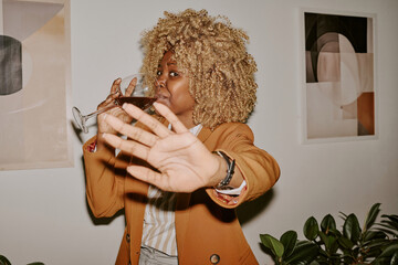 Curly haired woman trying to hide face while drinking red wine
