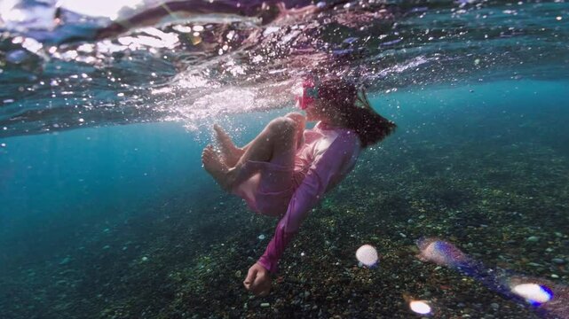 A baby girl dives and fools around underwater in glasses. Active recreation of swimming and snorkeling in the ocean. High quality 4k footage