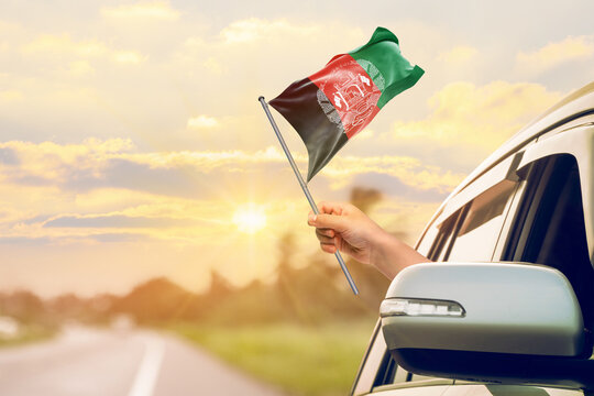 Waving the Afghanistan flag against the sunrise or sunset from a car driving along a country road. Holding the Afghanistan flag, traveling by car, on a weekend trip.
