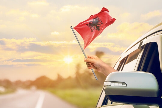 Waving the Albania flag against the sunrise or sunset from a car driving along a country road. Holding the Albania flag, traveling by car, on a weekend trip.