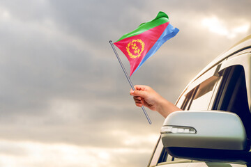 Waving the Eritrea flag against the sunrise or sunset from a car driving along a country road. Holding the Eritrea flag, traveling by car, on a weekend trip.