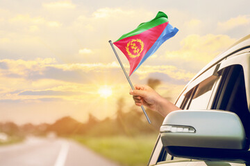 Waving the Eritrea flag against the sunrise or sunset from a car driving along a country road. Holding the Eritrea flag, traveling by car, on a weekend trip.