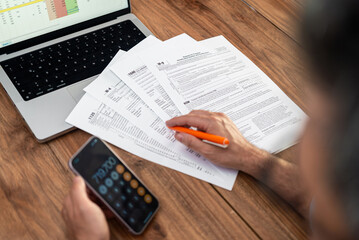 Male company accountant engages in filling tax forms correctly using calculator on smartphone for accurate financial data sitting at workplace with laptop