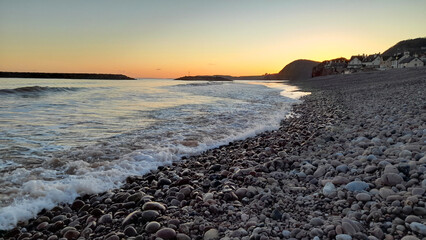 Small waves gently lapping the shore on the pebble beach at Sidmouth in Devon at sunset. 