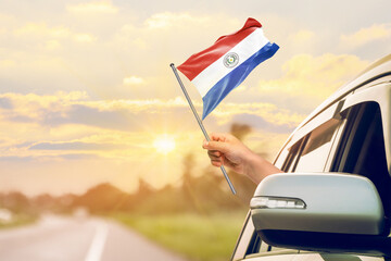 Waving the Paraguay flag against the sunrise or sunset from a car driving along a country road. Holding the Paraguay flag, traveling by car, on a weekend trip.