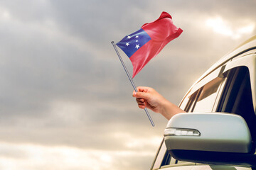 Waving the Samoa flag against the sunrise or sunset from a car driving along a country road. Holding the Samoa flag, traveling by car, on a weekend trip.