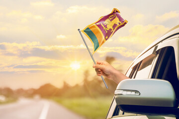 Waving the Sri Lanka flag against the sunrise or sunset from a car driving along a country road....