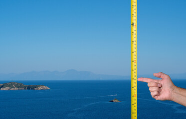 Rising sea level concept image as a hand points to a tape measure measuring the rising sea. Global...